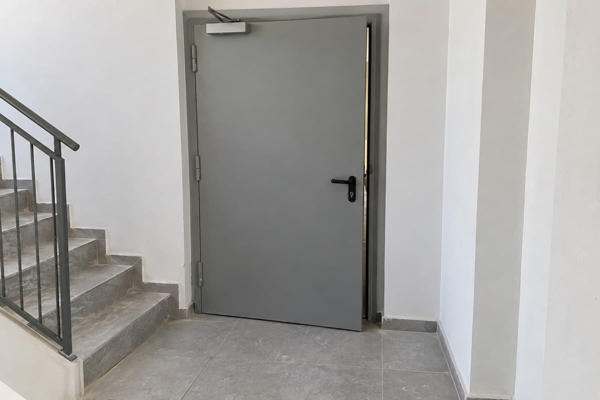 דלת אש בחדר מדרגות שלא נסגרת עד הסוף, עם מרווח בין הכנף למשקוף