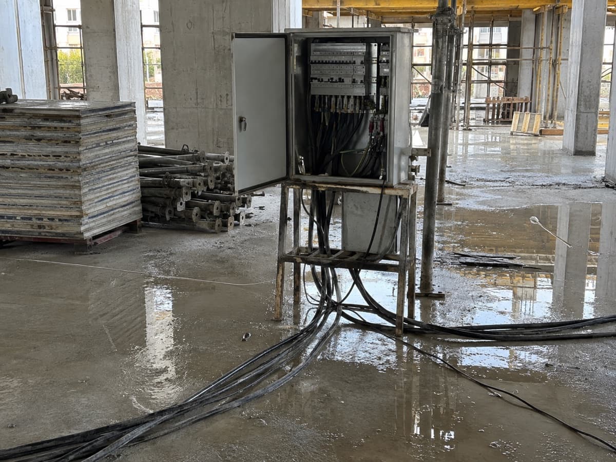 לוח חשמל זמני באתר בנייה עם דלת פתוחה וכבלים על רצפה רטובה