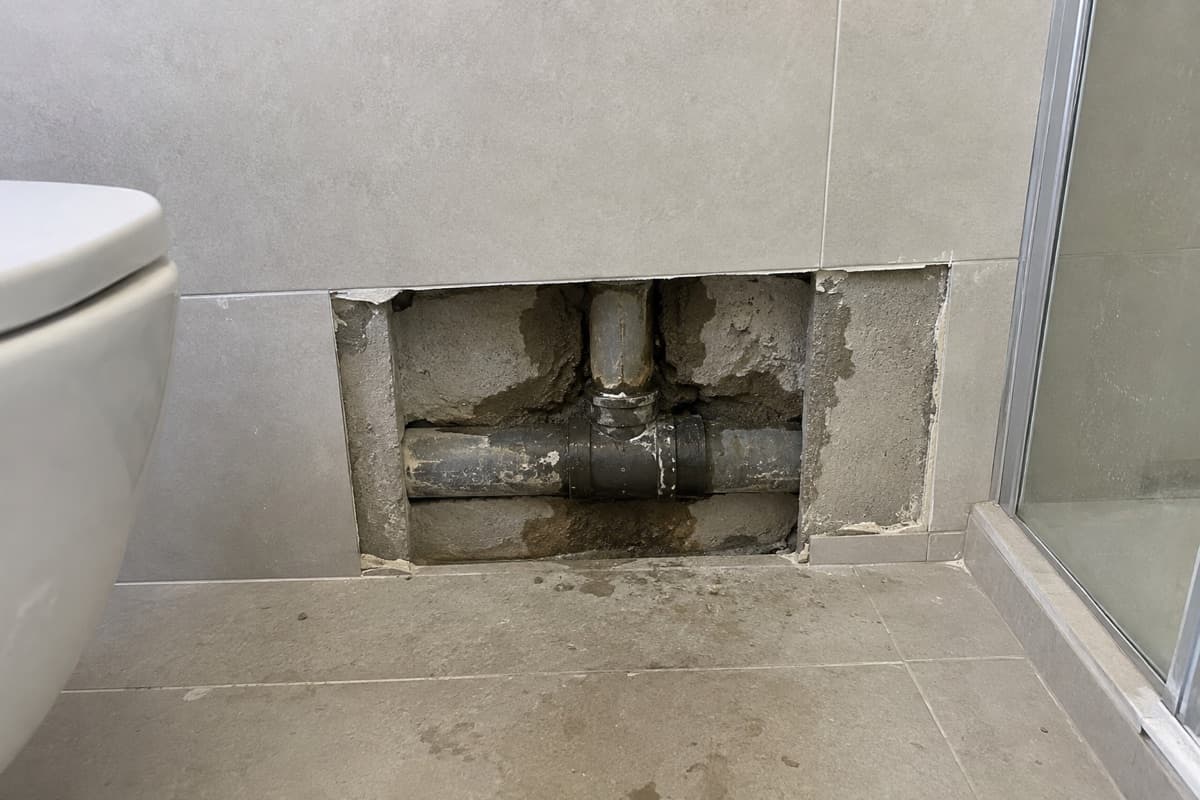 אריחים שפורקו בקיר חדר רחצה וחושפים חיבור צינור רטוב